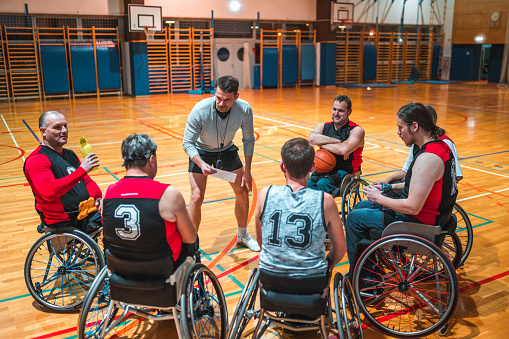 Coach giving play instructions for male wheelchair basketball team in a hall during time out.