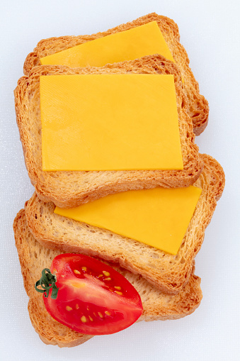 Four Biscotti Crackers with Cheddar Cheese and Tomato on White Cutting Board