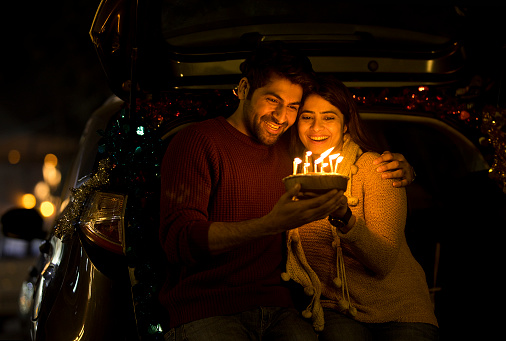 Cheerful couple celebrating birthday with cake in car trunk
