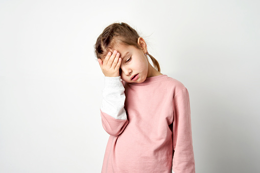 Cute child girl tired having headache, white background. Little girl holding her head with hands, stress and frustration concept.