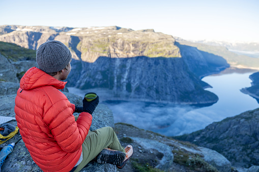 He sits on a cliff above a spectacular lake surrounded by mountains, Norway.