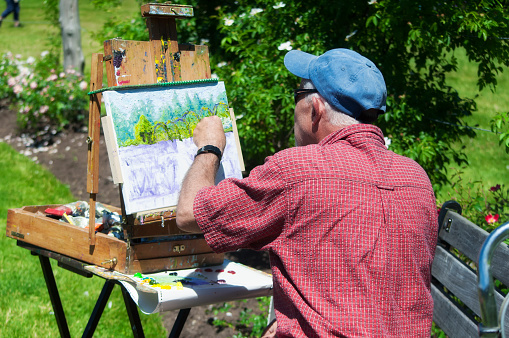 June 15, 2019.  West Hartford, Connecticut.  an older man painting the landscape in the summer rose garden at Elizabeth park in west hartford connecticut on a sunny day.