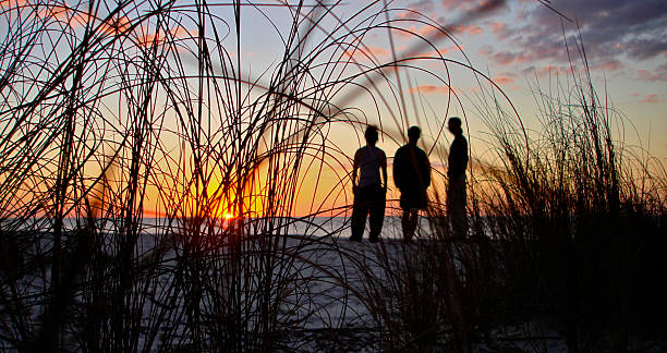 praia ao pôr-do-sol - silhouette three people beach horizon - fotografias e filmes do acervo