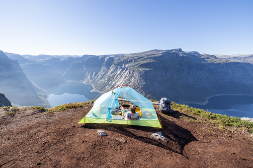 She stands beside the tent in the morning. Wild camping in the mountains in Norway in summer.