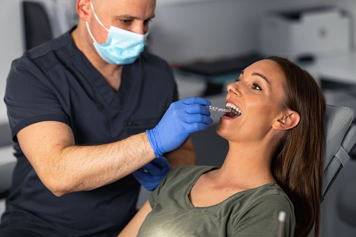 Shot of the dentist removing transparent trainer dental braces from the mouth of a young woman.