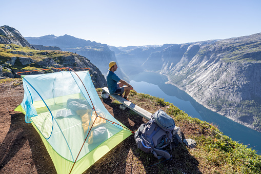 HE stands beside the tent in the morning. Wild camping in the mountains in Norway in summer.