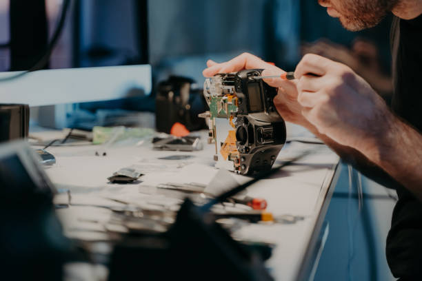 istock Woking process. Unknown man repairs professional digital camera, uses screwdriver, poses at workplace, holds photocamera disassembled part 1470252589