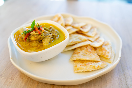 Crispy roti served with green curry with chicken on wooden table