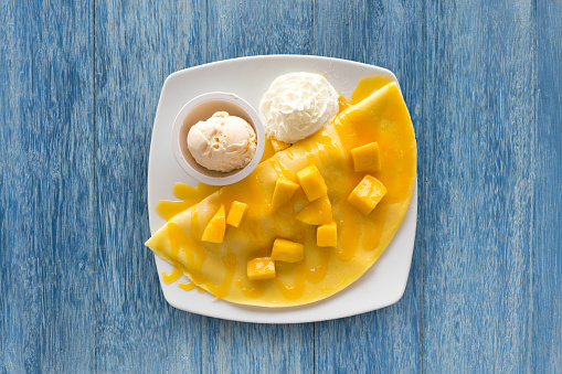 Refreshing Summer Dessert: Mango Crepe with Ice Cream on beautiful wooden blue table