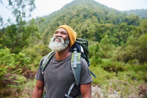 Smiling mature man with a backpack looking at the scenic view during a solo hike in some forested hills