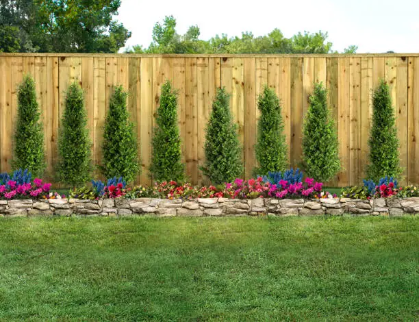 Photo of Empty backyard with green grass, trees, flowers and wood fence