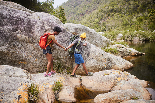Man giving his wife a helping hand while hiking together through a rocky ravine in the summertime