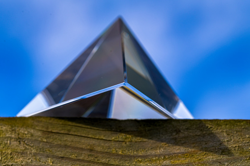 A glass triangular prism sitting on a wooden fence with a blue cloudy sky in the background perception