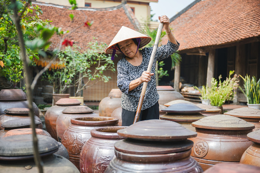Anciana vietnamita revolviendo en enorme vaina de soja de arcilla en el patio photo