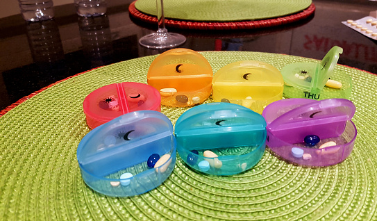Seven colorful containers for pills. Morning and night. One box for every day of the week.  Located on the kitchen table