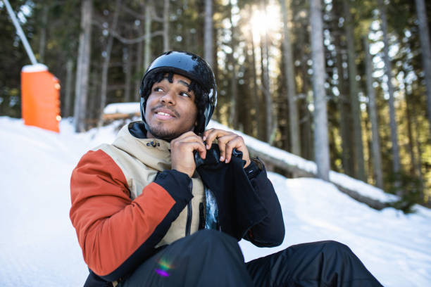 A young mixed-race man is putting on a helmet on a ski slope