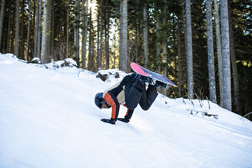 A young multiracial snowboarder is doing tricks on his snowboard on a ski slope