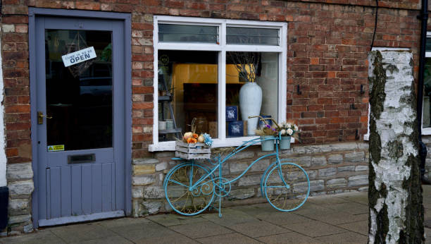 A flower shop with decorative bicycle outside displaying flowers A florist uses a painted up-cycled bicycle to attract customers to the shop in the town centre of Stratford upon Avon. The town is  nestled in the rural Warwickshire countryside, on the picturesque banks of the River Avon. It is a medieval market town and the birthplace of William Shakespeare, the world's greatest playwright. It is steeped in more than 800 years of Ye Olde English culture and history. historic heritage square phoenix stock pictures, royalty-free photos & images