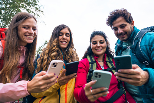 Four friends taking a break during their hike in mountain and checking maps on mobile phone.