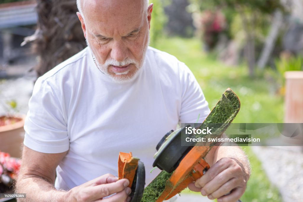 Senior man fixing lawn mower Man using gardening equipment Lawn Mower Stock Photo