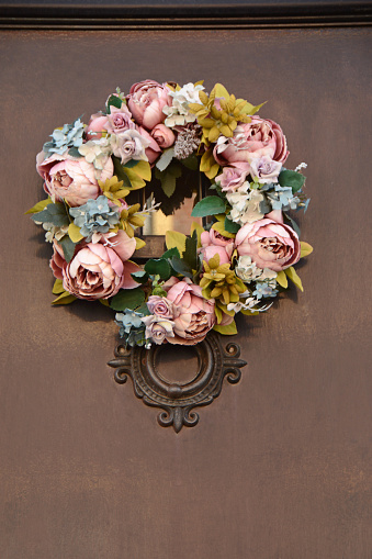 Single wreath hanging on a frontdoor.\nWreath made of artificial flowers like peony.