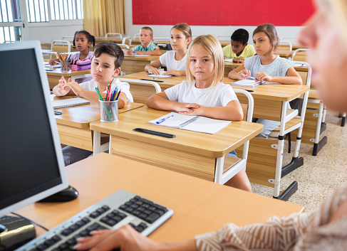 Portrait of diligent towheaded preteen girl looking at camera during lesson in primary school