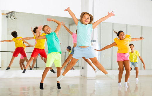 Group of happy sporty kids training in modern dance studio, jumping together
