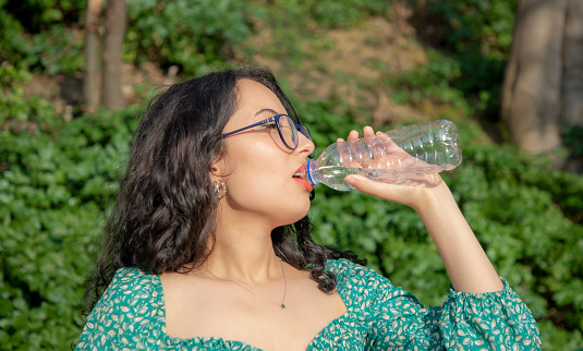 Young brunette woman with glasses is drinking water in nature