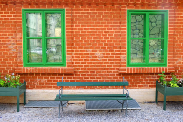 Cottage with brick wall, green windows, bench and colorful flowers.
