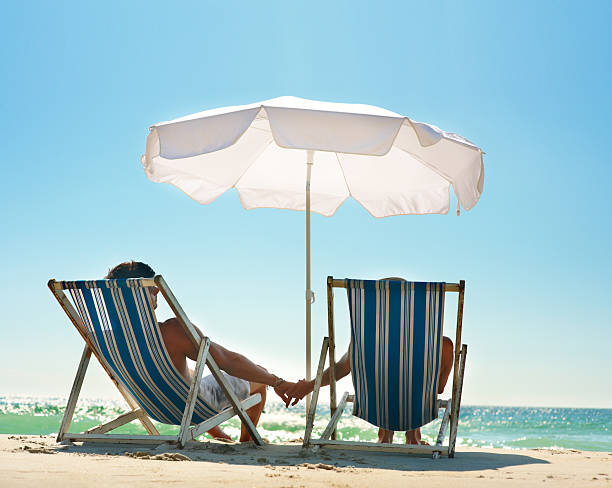istock Couple sitting on deck chairs under canopy at beach 147029221