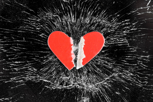 Broken love concept with torn paper heart on crashed glass smartphone touchscreen