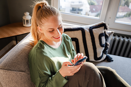 Young woman relaxing at home and using smart phone