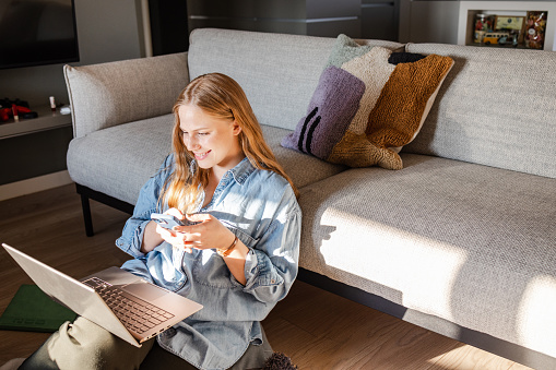 Young woman relaxing at home. She is using technology and smiling.