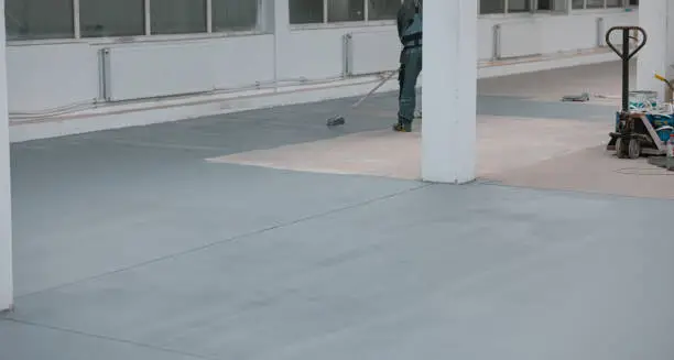 Photo of Worker paints the concrete floor with liquid gray paint