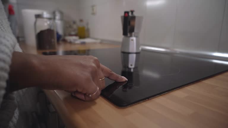 Unrecognisable black woman putting moka pot on the electric stove to make hot coffee at home.