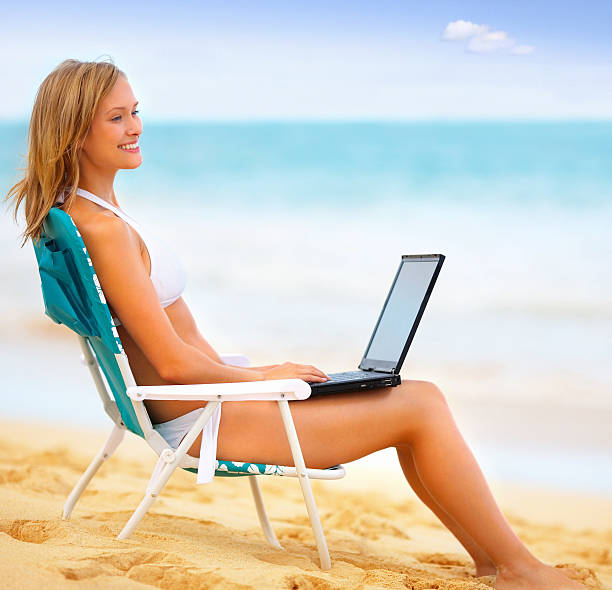 istock Side profile of young woman using laptop on the beach 147030330
