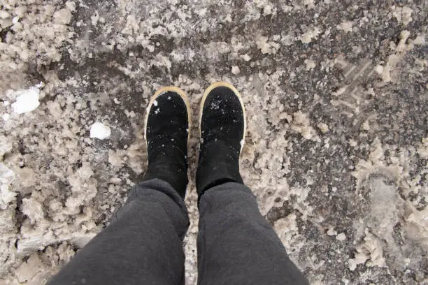 female legs in boots and gray pants on the road in wet snow in winter, feet on the road, path, winter bad weather