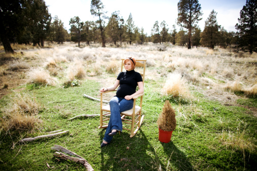 A photo of a young pregnant woman sitting in a rocking chair in a field.