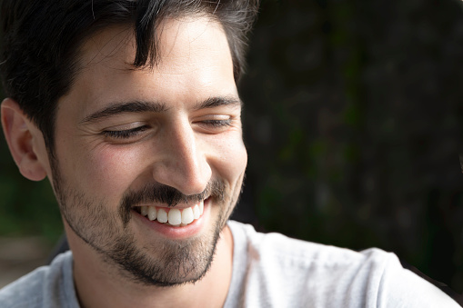 Portrait of a man laughing happily with a big casual smile on the street looking out. Beautiful smile of excited young man with perfect white teeth. Close up portrait of cheerful handsome man.