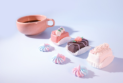 Coffee and Confections: A Pink Cup of Coffee with Mini Petite Four Decorated Cakes and Meringue Candy on Blue Background, Easter Treats, Bakery Concept