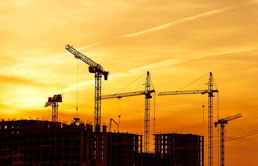 Tower cranes and new buildings silhouettes at construction site at yellow sky sunset. Shooting the building new houses in the city