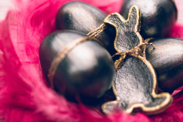 Close up of a dark metallic Easter bunny and Easter eggs surrounded by pink feathers. Color editing with added grain. Very selective and soft focus. Part of a series.