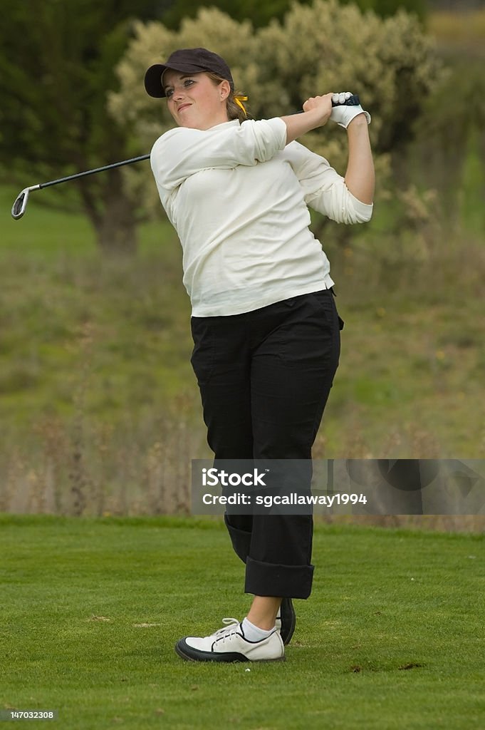 College golfer swing an iron golf club A young lady collegiate golfer is on the tee box of a par three swinging an iron club.  She was captured during her follow through. Activity Stock Photo