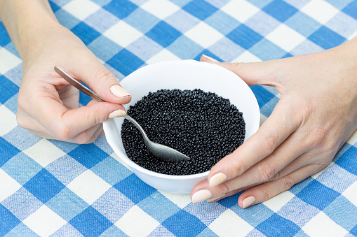 Woman eats black caviar from a white plate with a spoon.