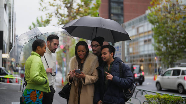 gruppo multirazziale di amici turisti che utilizzano lo smartphone per esplorare la città di harajuku tokyo - candid women african descent umbrella foto e immagini stock