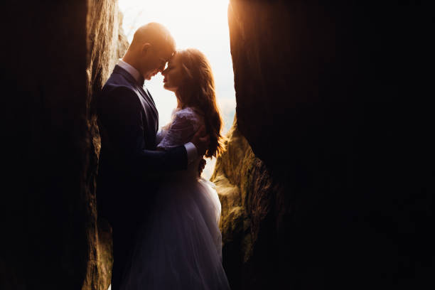 A romantic couple is hugging and standing among the rocks on the background of the sunset somewhere far away in the mountains