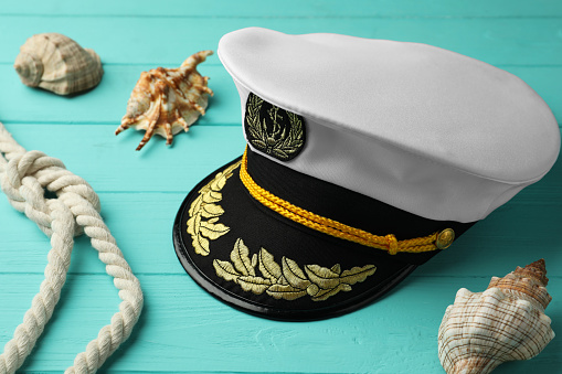Peaked cap, rope and shells on turquoise wooden background