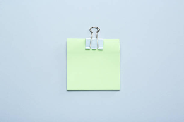 istock Blank light green note with white paper clamp on grey background, top view. Space for text 1470331126
