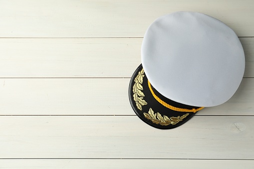 Peaked cap with accessories on white wooden background, top view. Space for text