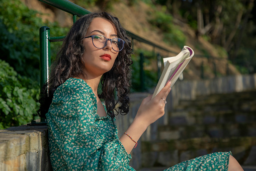 Young woman with brunette glasses reading a book outside